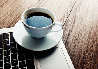 Cup of coffee and laptop on wooden table.