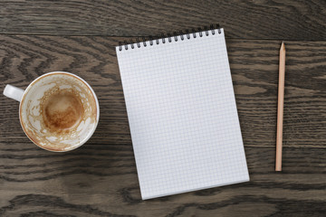 Blank notepad with pencil and empty coffee cup on wooden table