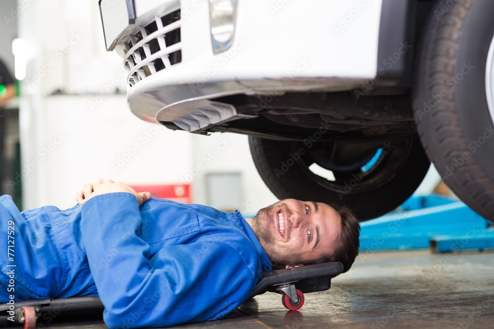 Poster smiling mechanic lying on trolley