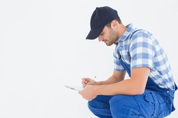 Handyman crouching while writing on clipboard