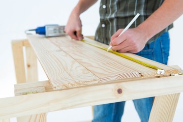 Carpenter marking with measure tape on wooden plank