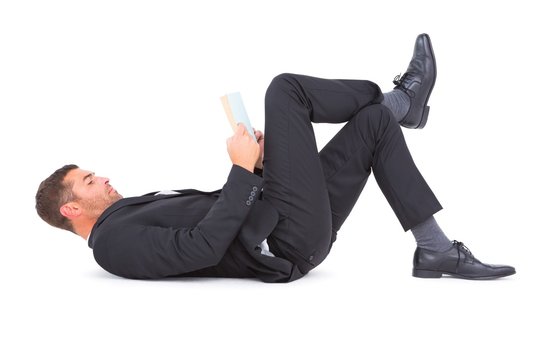 Businessman lying on the floor reading book