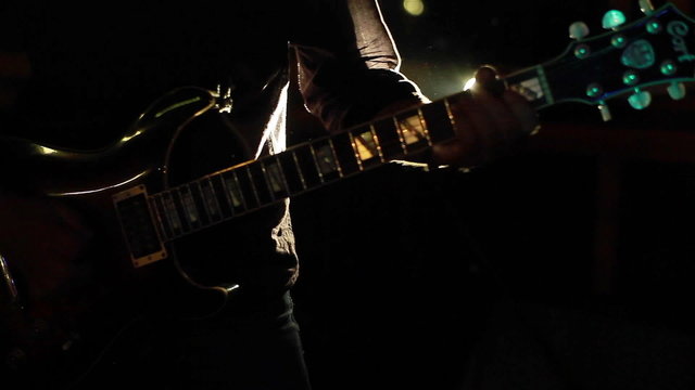 Musician playing guitar in club in a backlight