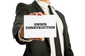 Businessman in a suit holding up a business card saying Under co