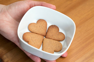 A hand holding white bowl with heart-shaped cookies