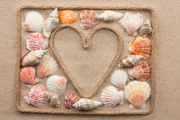 Symbolic heart made from rope and sea shells lying on the sand