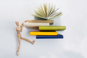 Wooden mannequin tries to get up the stack of colorful books