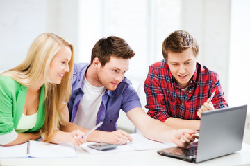 smiling students looking at laptop at school