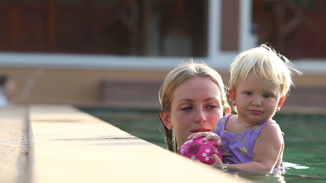Mom puts small blonde child on the edge of swimming pool	