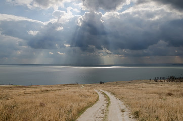 Dirt road leading to the sea and the dramatic clouds over the se