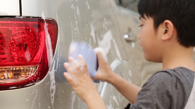 Asian cute boy washing car . Child helping family clean big car.
