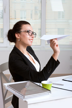Woman in a suit sitting at table in office throwing paper airpla