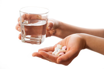 Hands holding a glass of water and bunch of pills