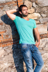 casual man stands against a brick rock wall, hand in pocket