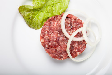 Raw steak with onion rings and green salad on a white plate