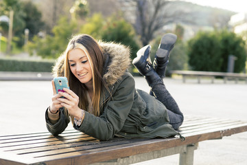 Happines beautiful girl with smart phone lying on the bench.