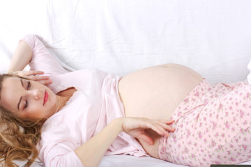 young pregnant woman luxuriates in a white bed.