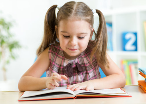 Cute kid girl reading story from big book in nursery
