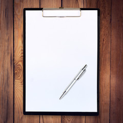 white paper clipboard on wood background with pen