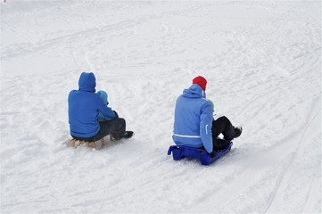 Familie am Schlitteln in blauen Schneeanzügen