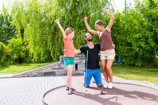 Familie spielt drau&szlig;en zusammen Minigolf