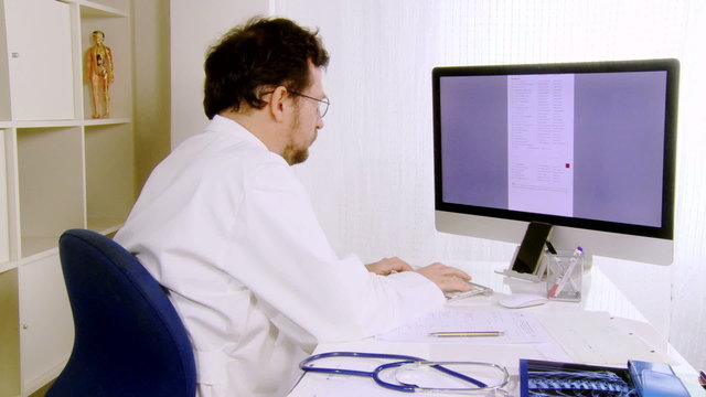 Doctor working in office at computer thumb up