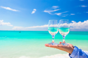 Closeup of wineglasses in hand on the white sandy beach