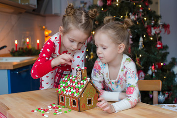 Little adorable girls decorating gingerbread house for Christmas