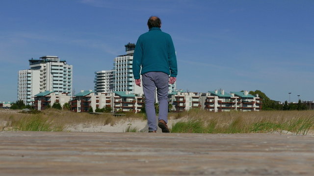 A Man Walks by a Wooden Walkway to Town, view from the back