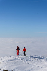 Two skiers on top of mountain above the clouds