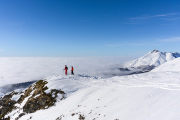 Naklejka na ściany i meble Two skiers on top of mountain above the clouds