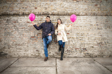 Fototapeta na wymiar Young couple leaning on the wall holding pink balloons.