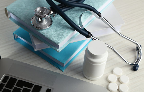 Medical stethoscope with books and laptop on wooden table