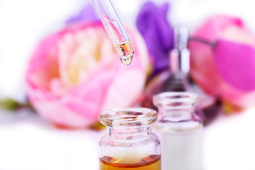 Dropper bottle of perfume with flowers on light background