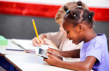 Multi ethnic primary students playing with tablet and writing