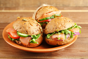 Sandwiches with salmon on plate, on wooden background
