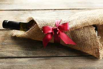 Wine bottle wrapped in burlap cloth on wooden planks background