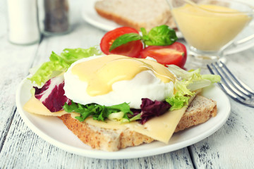Toast with egg Benedict and tomato on plate on wooden table