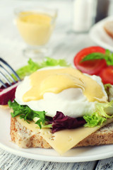 Toast with egg Benedict and tomato on plate on wooden table