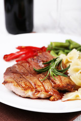 Steak with vegetables and pasta on plate on wooden plate