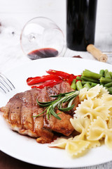 Steak with vegetables and pasta on plate on wooden plate