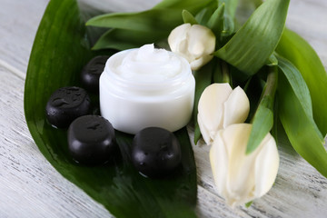 Cosmetic cream with flowers and spa stones on wooden background