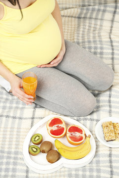 Young pregnant woman sitting on sofa with breakfast, top view