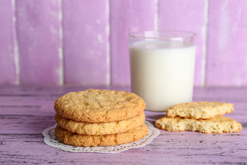 Tasty cookies and glass of milk on color wooden background