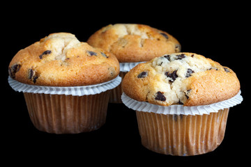 Three light chocolate chip muffins in wax liner on black.
