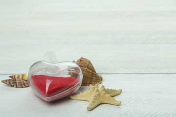seashells and a heart in the sand on the wooden background