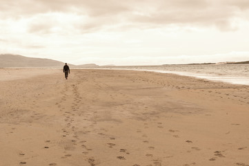 Fototapeta na wymiar Solitary man taken from behind walking in an empty beach.