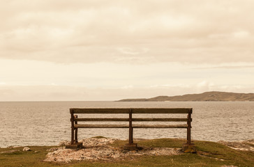 Fototapeta na wymiar Old bench facing an open view with sea and faraway mountains.