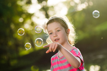 Little girl is playing with soap bubbles