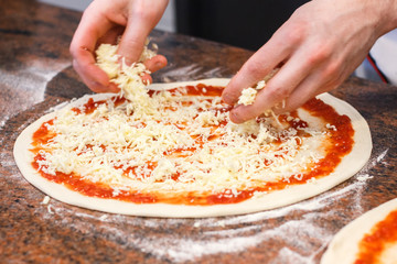 Cheese being spread on tomato sauce on pizza base. - obrazy, fototapety, plakaty